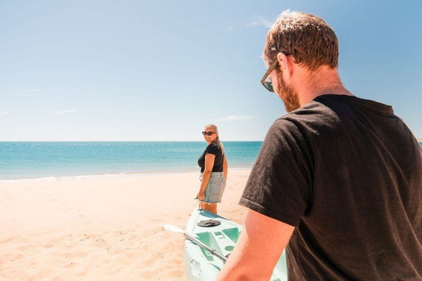 A beach scene with a person holding a surfboard and another person standing in the background. 5