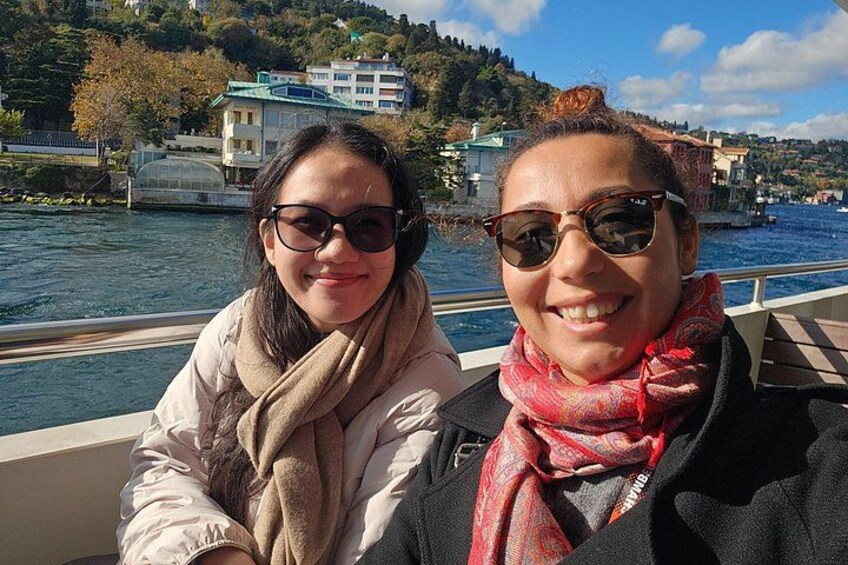 Deux personnes se trouvent sur un bateau, avec une rivière et des bâtiments en arrière-plan. 3