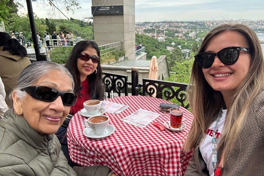 Trois personnes sont assises à une table recouverte d’une nappe à carreaux rouges et blancs, et savourent un café et un thé. 3