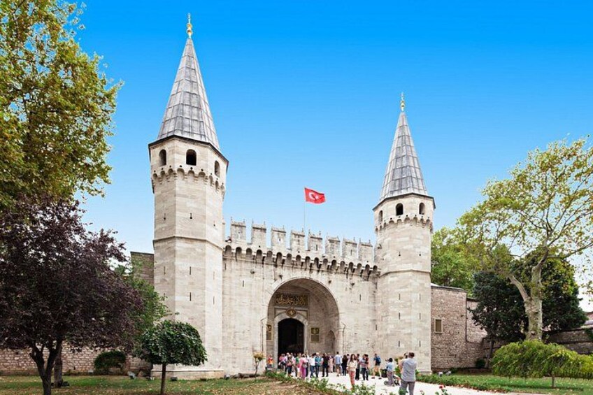 A historic stone gate with two towers, a clear blue sky, and a flag. 2