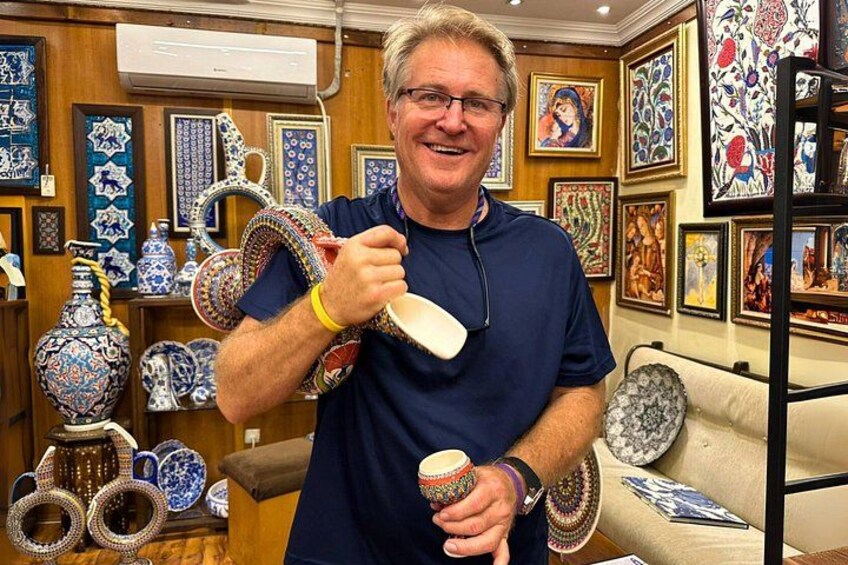Une personne tenant une tasse en céramique dans une pièce où sont exposées diverses pièces de poterie et œuvres d’art. 2