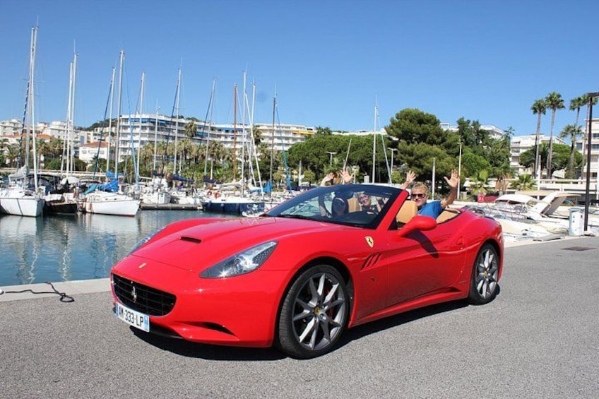 A red convertible sports car parked by a marina with boats and buildings in the background. 2