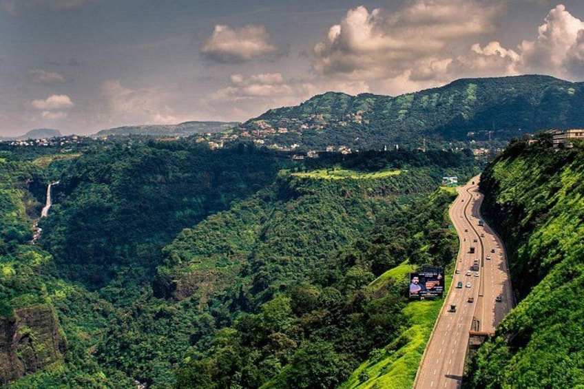 A winding highway through a lush valley with a waterfall in the distance. 2