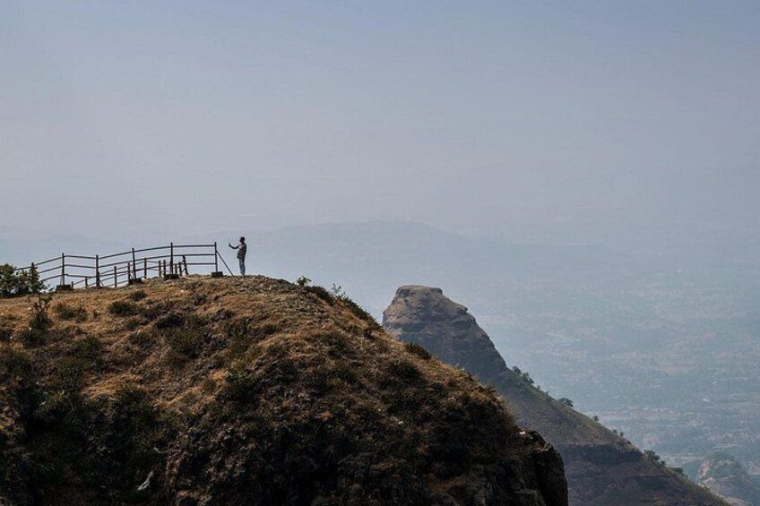 A person standing on a hill with a fence, overlooking a valley and distant mountains. 3