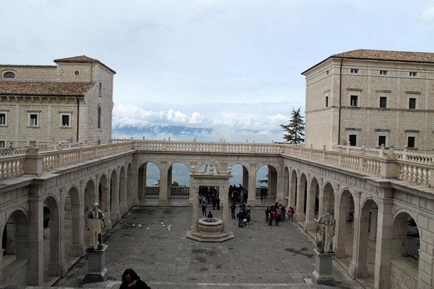 A historic courtyard with arches, a fountain, and people walking. 1