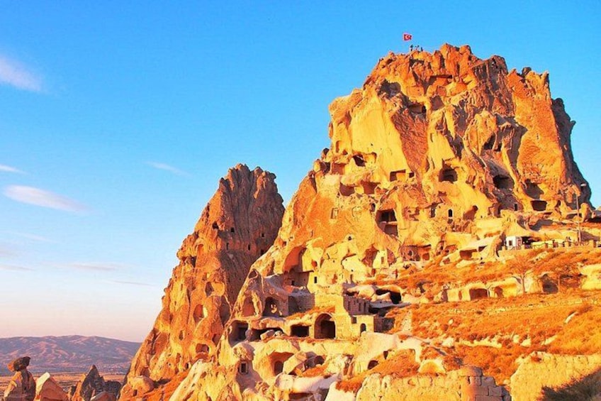 A rocky mountain with cave dwellings and a flag on top. 5