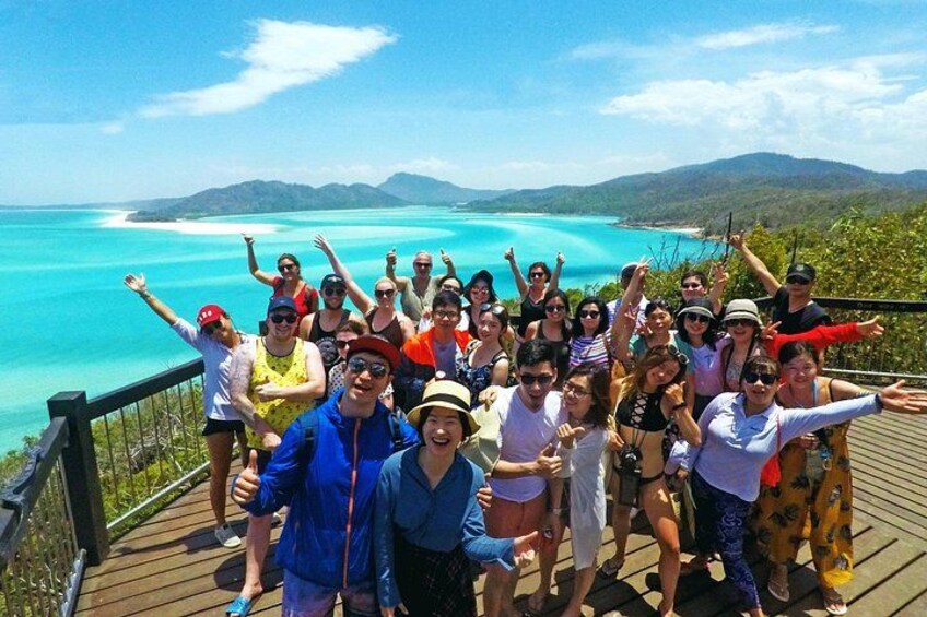A group of people on a wooden deck overlooking a turquoise sea and distant mountains. 2