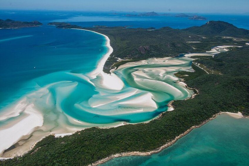 An aerial view of a coastal landscape with white sand beaches, turquoise waters, and green vegetation. 4