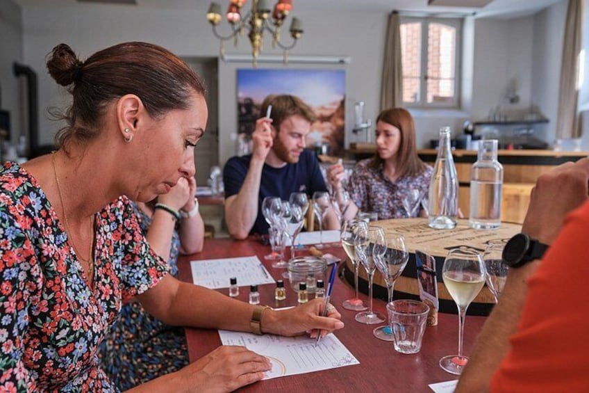 Un grupo de personas sentadas en una mesa con copas de vino y una botella, participando en una degustación. 3
