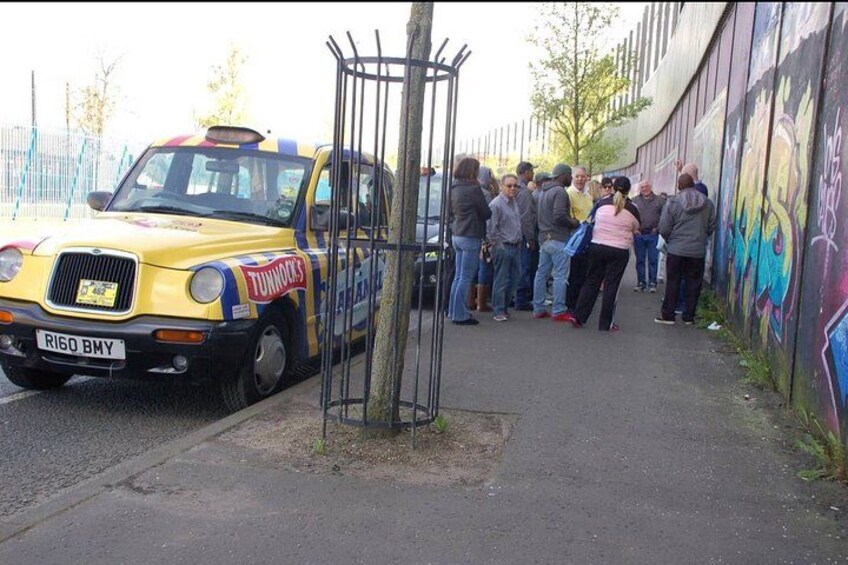 A yellow taxi with 'TUNINGS' written on it, parked on a street with a group of people standing nearby. 3