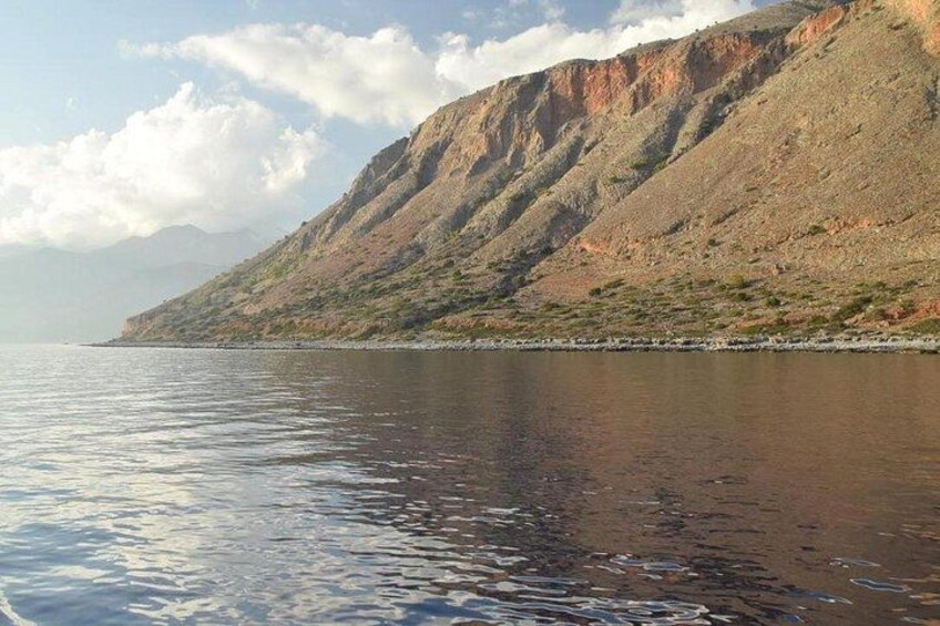 Un cuerpo de agua tranquila que refleja el cielo, una costa rocosa y una cadena montañosa al fondo. 2