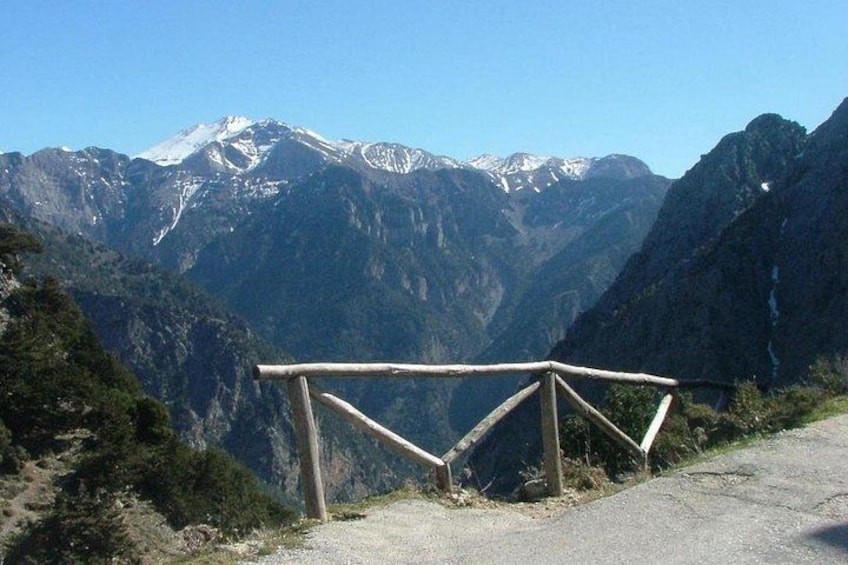 Une route de montagne bordée d’une rambarde en bois, avec des sommets enneigés en arrière-plan. 3