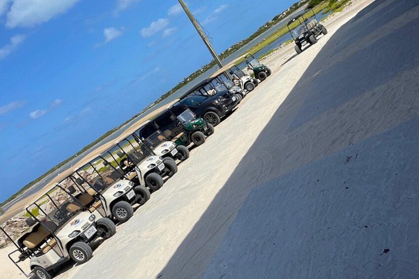 A line of off-road vehicles parked on a concrete surface with a clear sky and a distant shoreline. 3