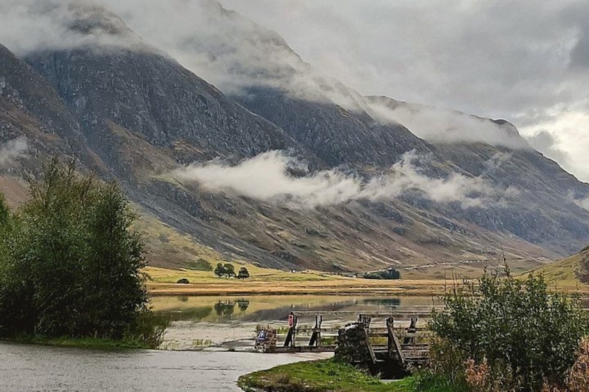 A mountainous landscape with a lake, a wooden bridge, and a few trees. 2