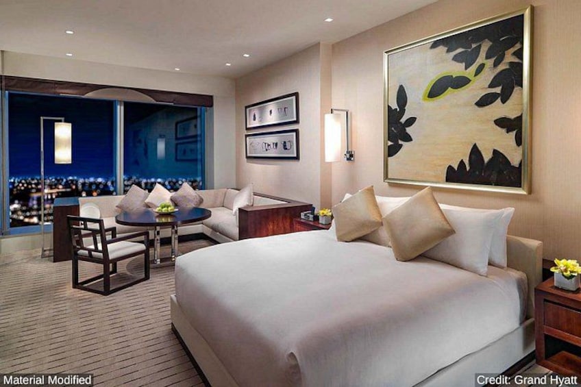 A modern hotel room with a large bed, a desk, and a view of the city at night. 2