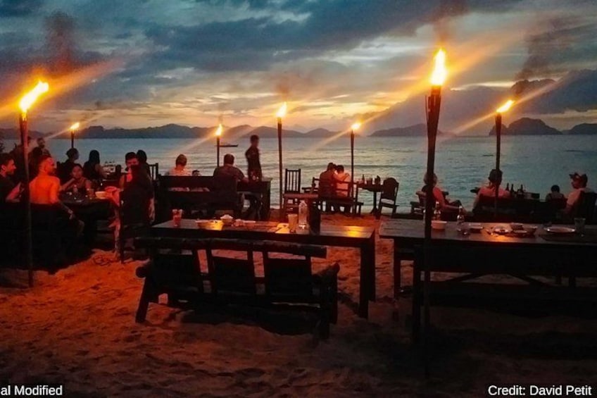 A beachside restaurant with tables and chairs, lit by torches, overlooking the sea. 5
