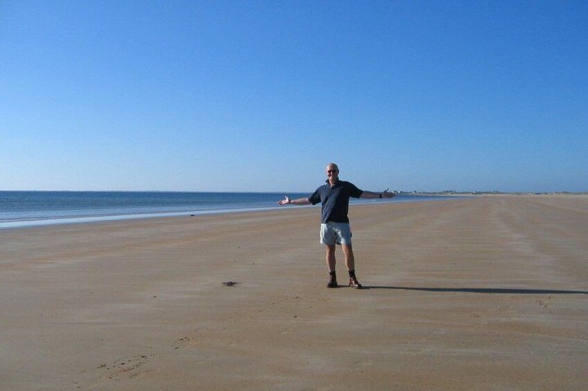 A person standing on a sandy beach with the ocean in the background. 3