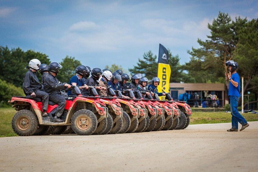 A group of people on ATVs lined up on a road with a flag and a building in the background. 2