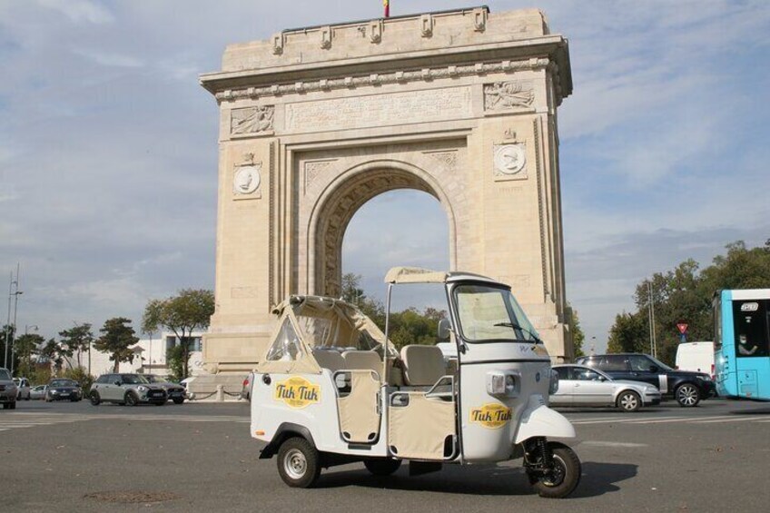 A tuk-tuk parked in front of a large archway. 2