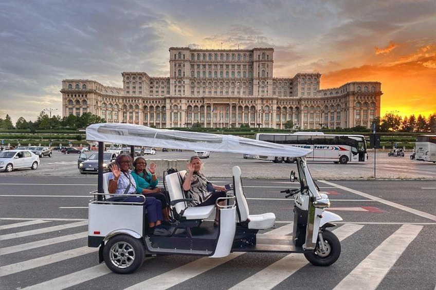 Une voiturette de golf blanche, avec des passagers à bord, est garée sur un parking, avec un grand bâtiment en arrière-plan. 1
