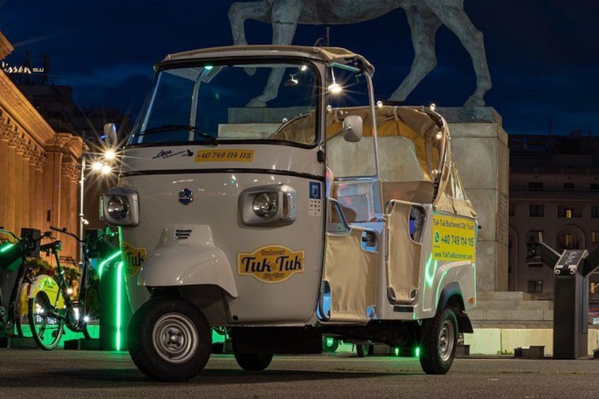 A tuk-tuk with a sign, parked in front of a building with a large sculpture. 4