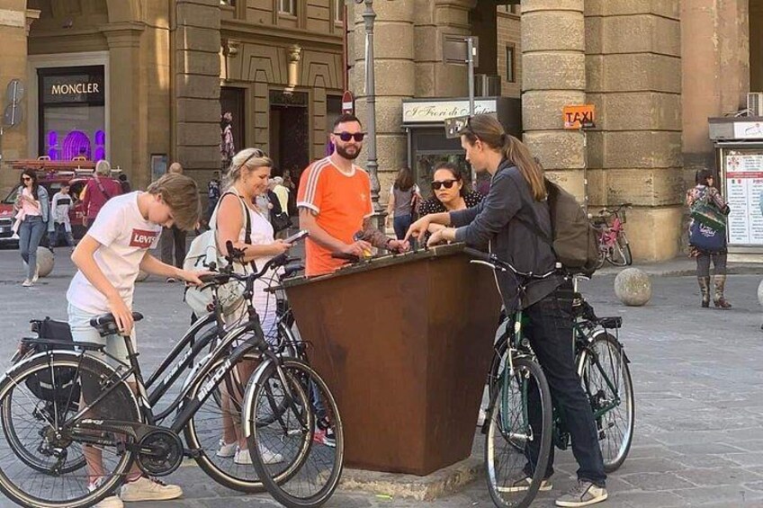 A group of people interacting at a wooden kiosk on a city street, with bicycles parked nearby. 2