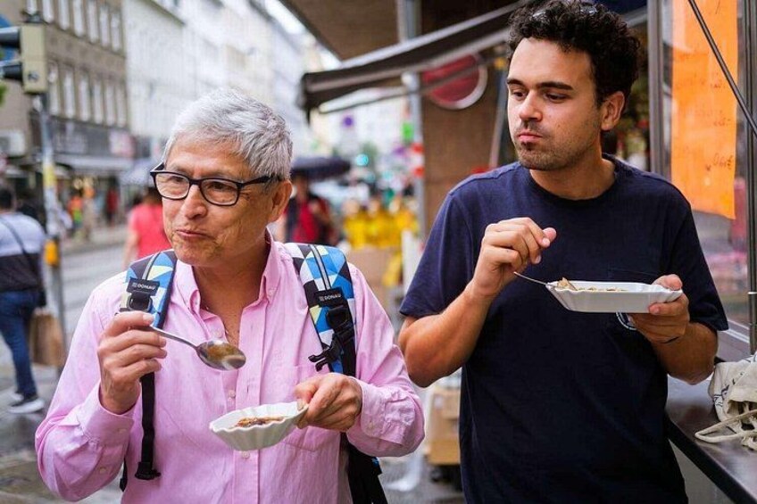 Zwei Personen essen an einem Essensstand draußen. 3