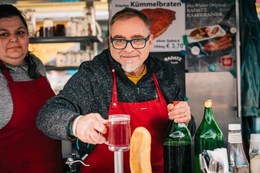 En person hælder væske i et glas, med flasker og en baguette på disken. 3