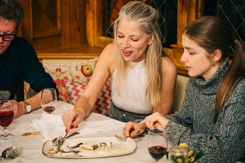 Drei Personen essen an einem Tisch, mit einem Teller Essen, Weingläsern und Besteck. 2