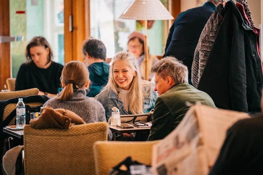 People sitting at tables in a cafe with wicker chairs and a lamp. 2