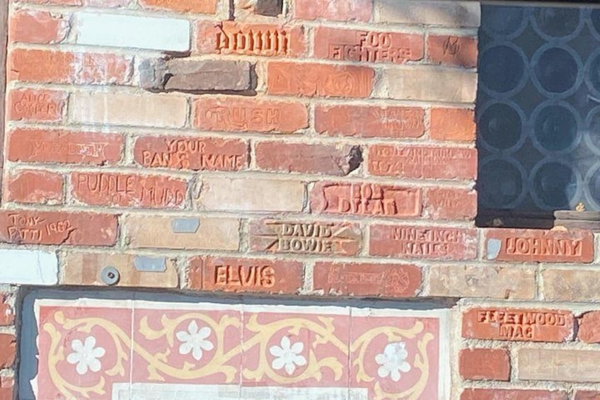 A brick wall with names and phrases like 'Elvis' and 'Your Bar's Mate' carved into it. 2