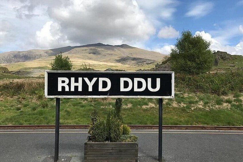 Un panneau de signalisation routière indiquant « RHYD DDU », dans un paysage rural avec des collines et un ciel dégagé. 4