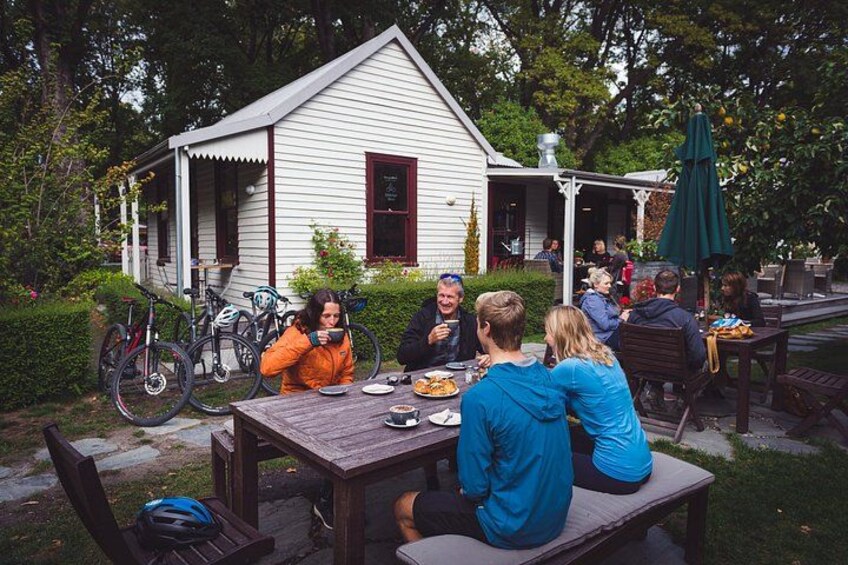 Un gruppo di persone cena all'aperto a un tavolo di legno, con delle biciclette parcheggiate nelle vicinanze. 3
