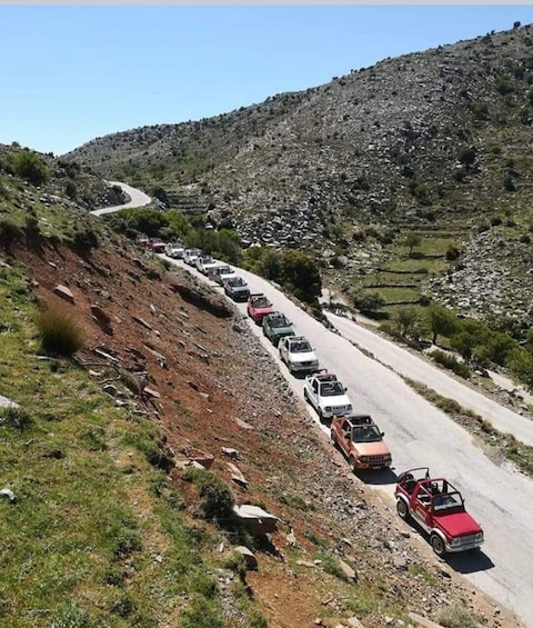 A winding road with a line of cars parked along the side. 1