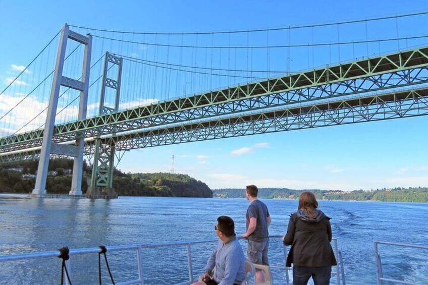 A large suspension bridge over a body of water with three people on a boat. 4