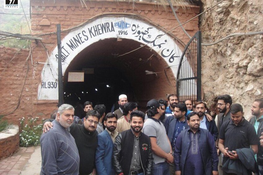 Un grupo de personas de pie frente a la entrada de un túnel con la leyenda 'Salt Mines Khewra'. 1