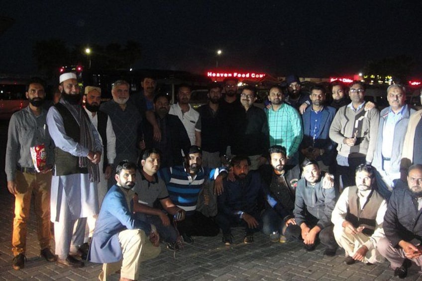 Un grupo de personas reunidas al aire libre de noche, con un cartel en el fondo que dice 'Heaven Food Court'. 5