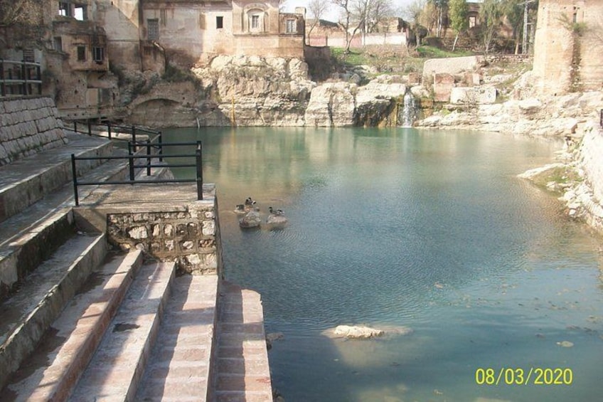 Un río con escalones que bajan al agua, patos nadando y edificios de piedra al fondo. 4