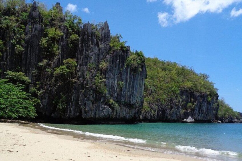 A beach with clear turquoise water, a sandy shore, and a rocky cliff with dense vegetation. 2