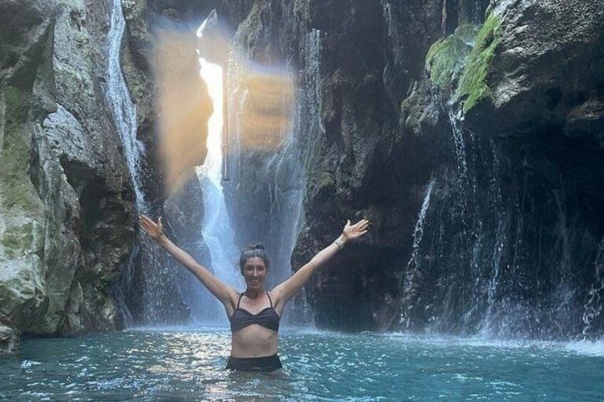 Een persoon staat in het water, met armen omhoog, voor een waterval. 2