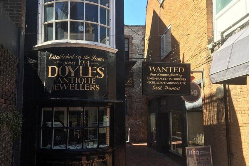 Una calle con una tienda llamada 'Doyles Antique Jewellers' y otra tienda con un letrero que anuncia artículos 'Wanted'. 3