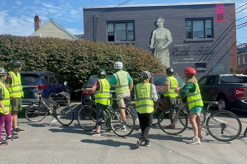 A group of people on bicycles in a parking lot with a mural in the background. 4