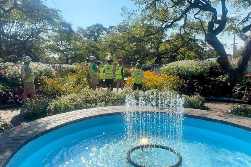 A circular fountain with water jets in a garden with people in safety vests. 3