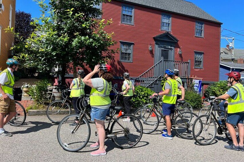 A group of cyclists wearing safety vests standing in front of a red building. 2