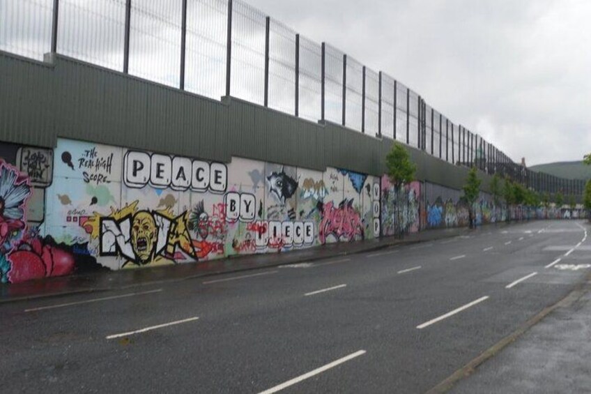 Una strada con un muro imbrattato di graffiti e una recinzione metallica. 3