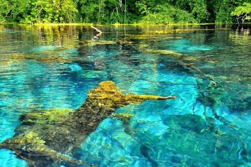 A clear river with a large rock formation in the water. 3