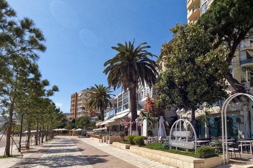 A sunny street lined with palm trees, outdoor cafes, and a clear blue sky. 5