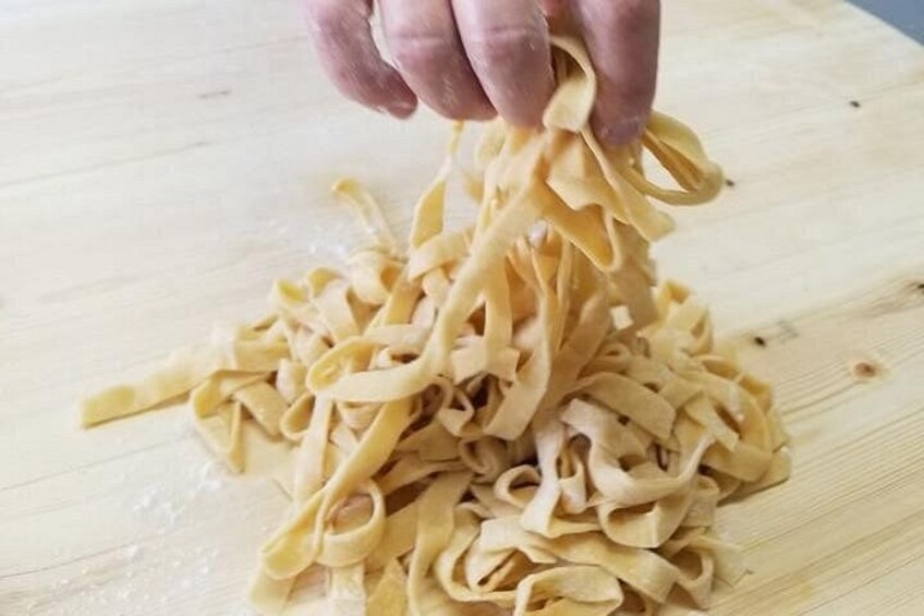 Una tabla de madera con pasta y una mano sosteniendo pasta. 2