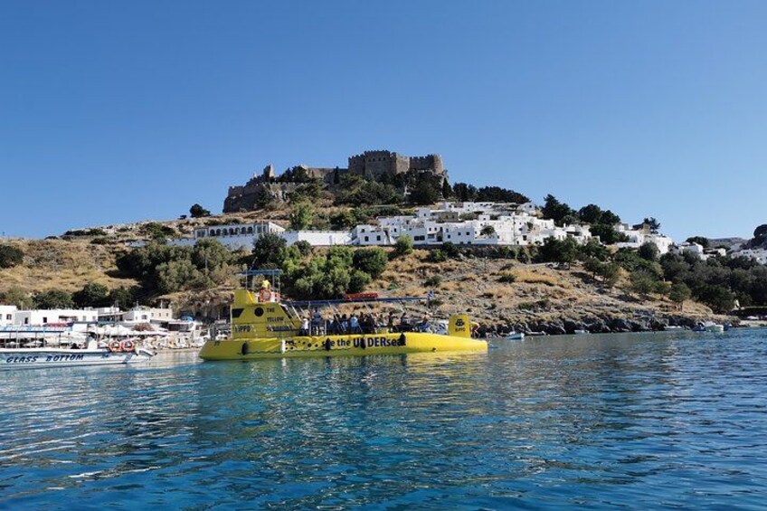 A yellow boat with passengers, a castle on a hill, and white buildings along the coast. 5