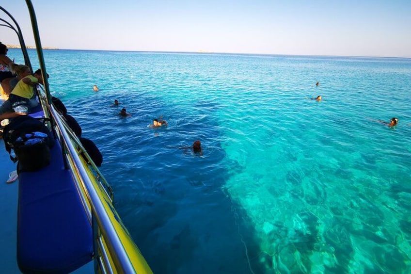 A boat with people swimming in the clear blue sea. 2